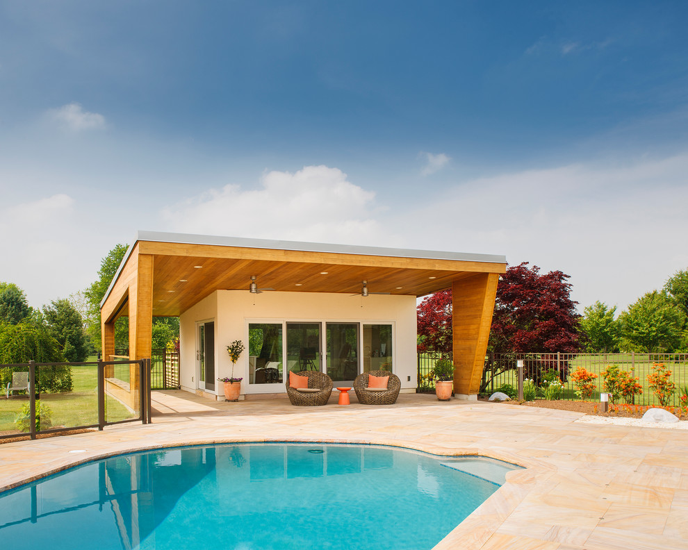 Стильный дизайн: большой бассейн в форме фасоли на заднем дворе в современном стиле с домиком у бассейна и покрытием из каменной брусчатки - последний тренд