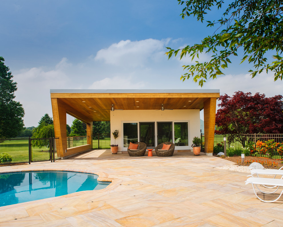 Large contemporary back kidney-shaped swimming pool in Philadelphia with a pool house and natural stone paving.