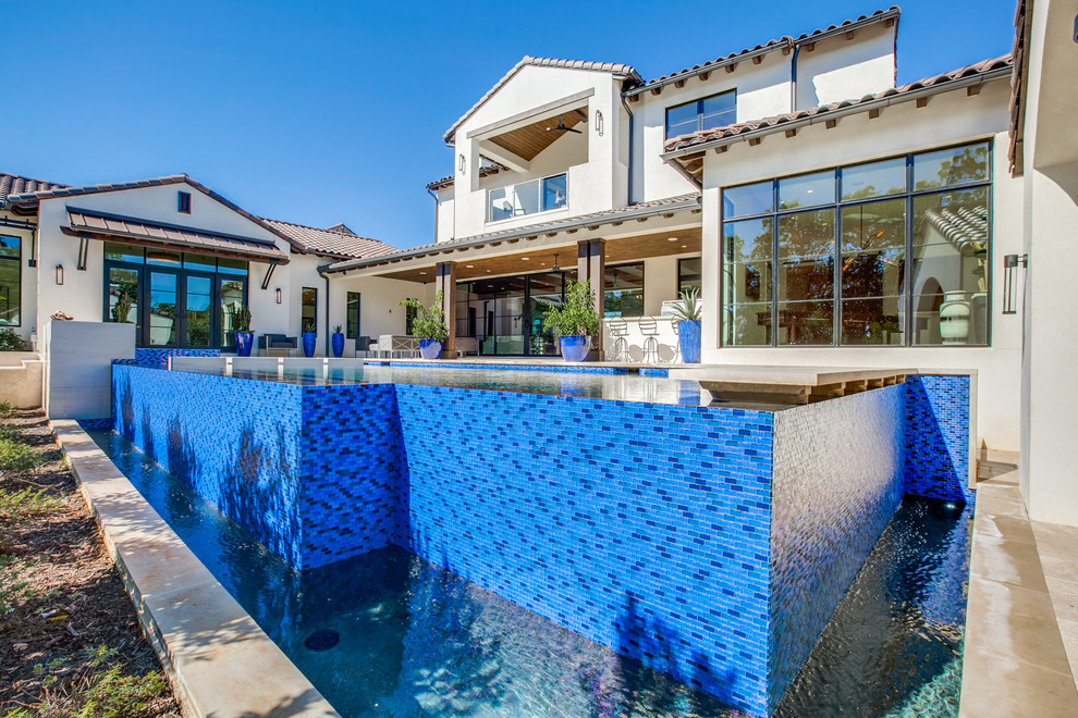 Foto di una grande piscina a sfioro infinito mediterranea rettangolare dietro casa con una vasca idromassaggio e pavimentazioni in pietra naturale