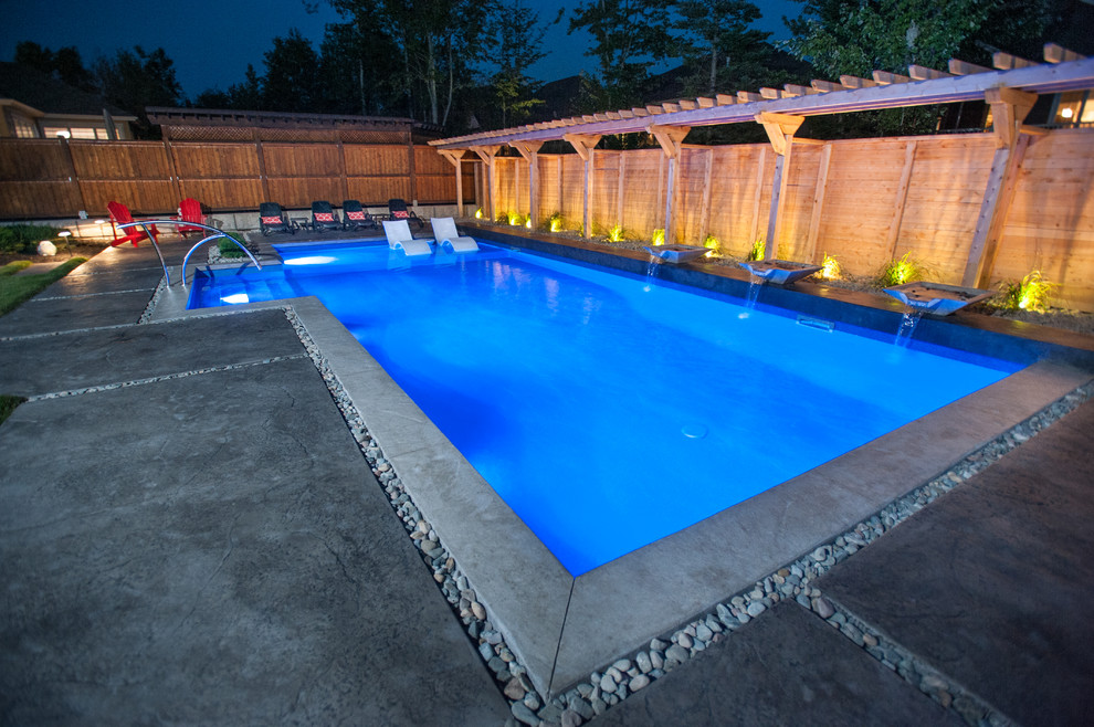 Ejemplo de piscina con fuente alargada actual grande a medida en patio trasero con suelo de hormigón estampado