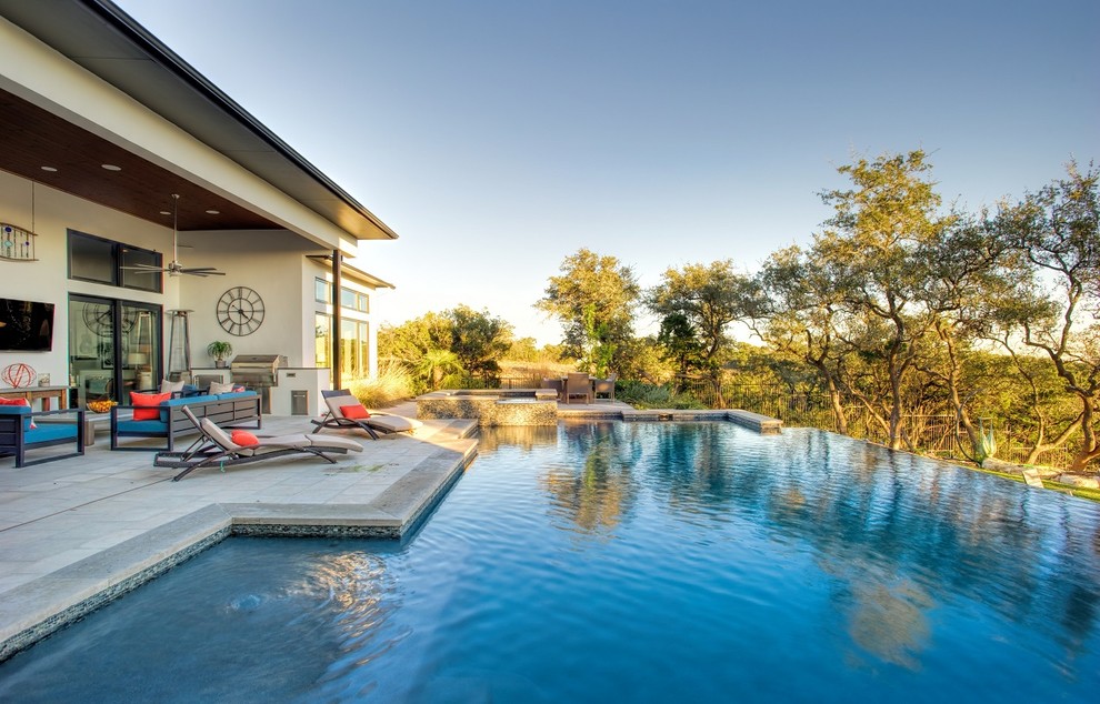 Modelo de casa de la piscina y piscina infinita actual grande rectangular en patio trasero con adoquines de piedra natural