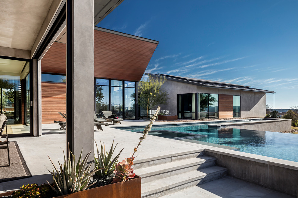 Ispirazione per una piscina a sfioro infinito design personalizzata dietro casa con una vasca idromassaggio e lastre di cemento