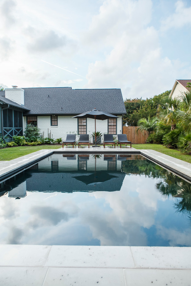 Modelo de casa de la piscina y piscina actual de tamaño medio rectangular en patio trasero con adoquines de hormigón