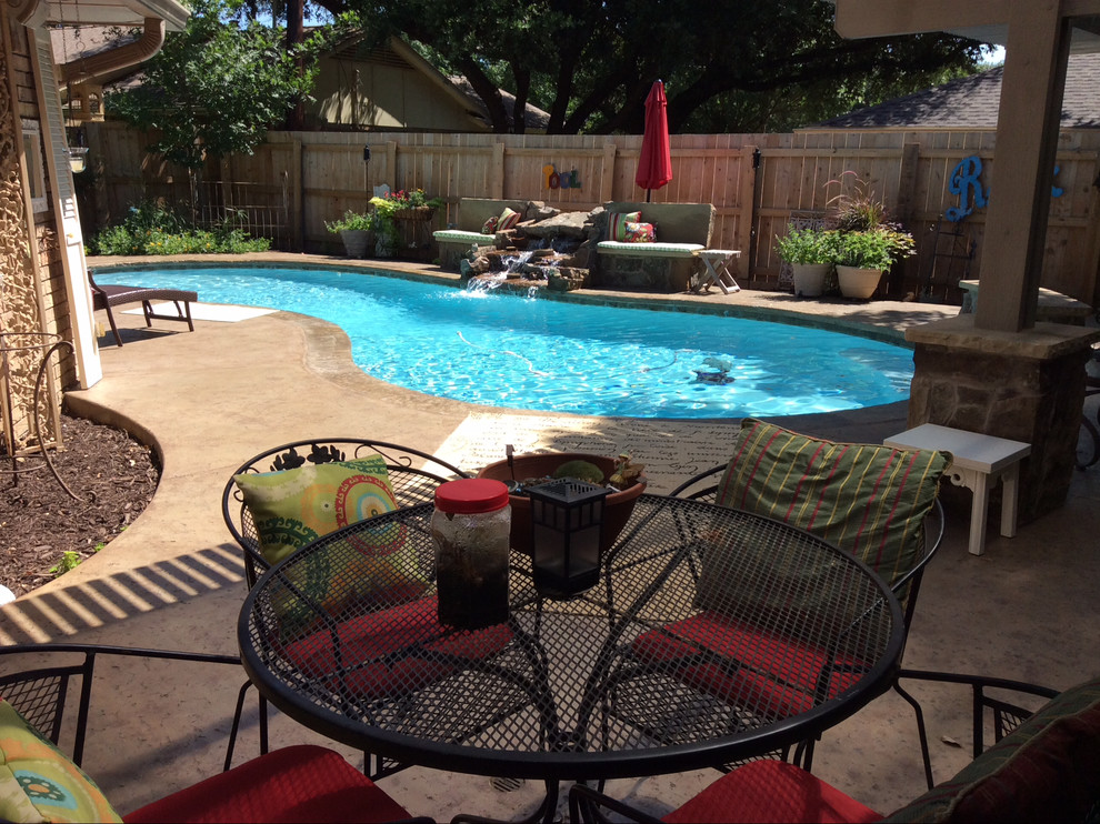 Mittelgroßer Uriger Schwimmteich hinter dem Haus in Nierenform mit Stempelbeton und Wasserspiel in Dallas