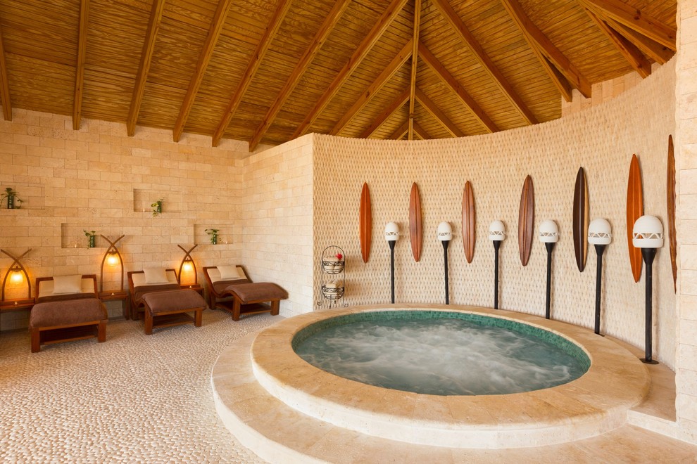Immagine di una piccola piscina coperta tropicale rotonda con una vasca idromassaggio e pavimentazioni in pietra naturale