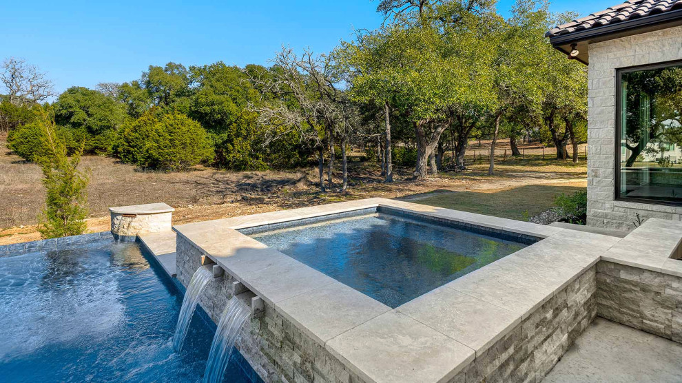 This is an example of a large classic back rectangular infinity swimming pool in Austin with concrete slabs.