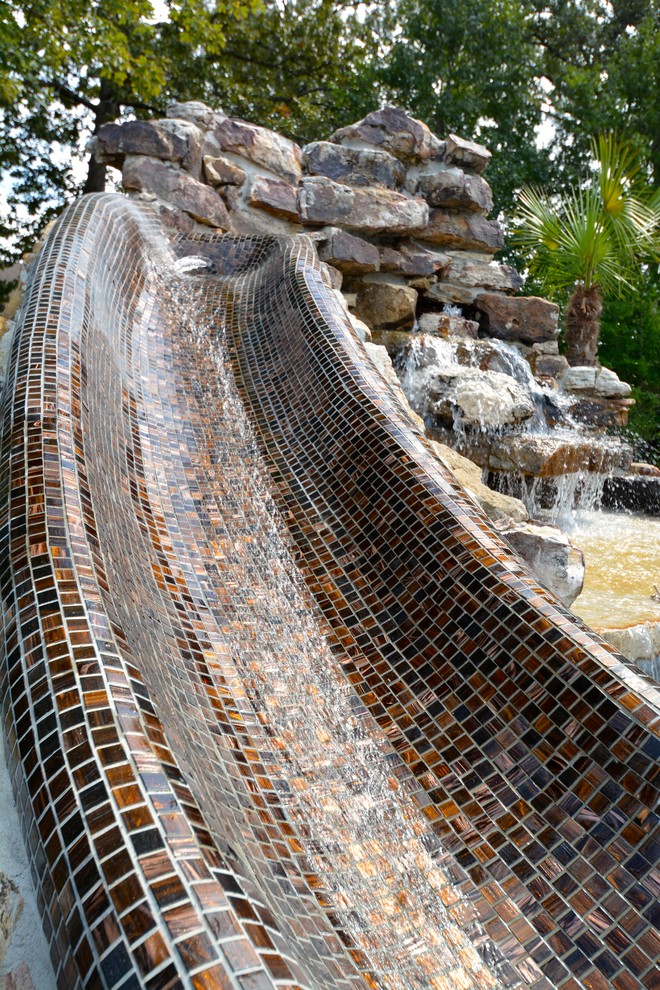 Medium sized rustic back custom shaped lengths swimming pool in Little Rock with a water slide and natural stone paving.