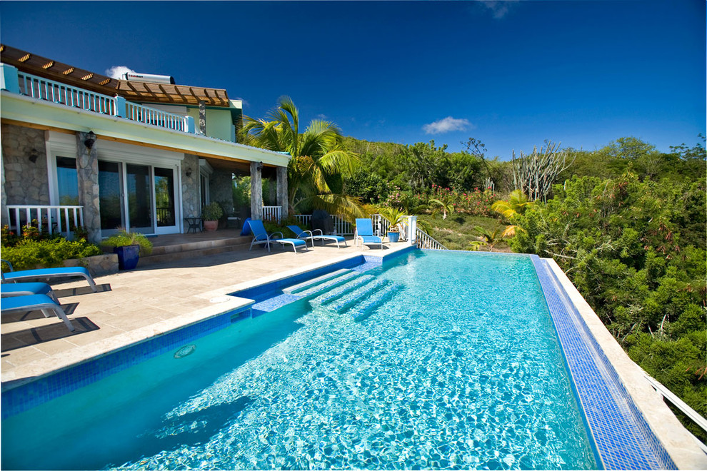 Ejemplo de piscina infinita tropical rectangular en patio trasero con suelo de baldosas