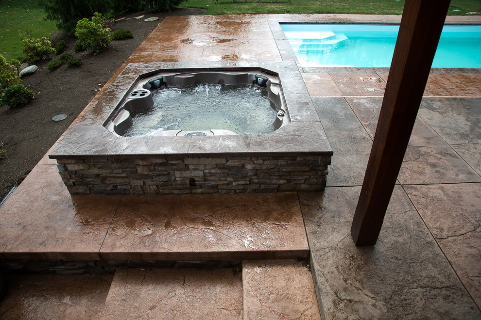 Exempel på en liten lantlig pool på baksidan av huset, med spabad och stämplad betong
