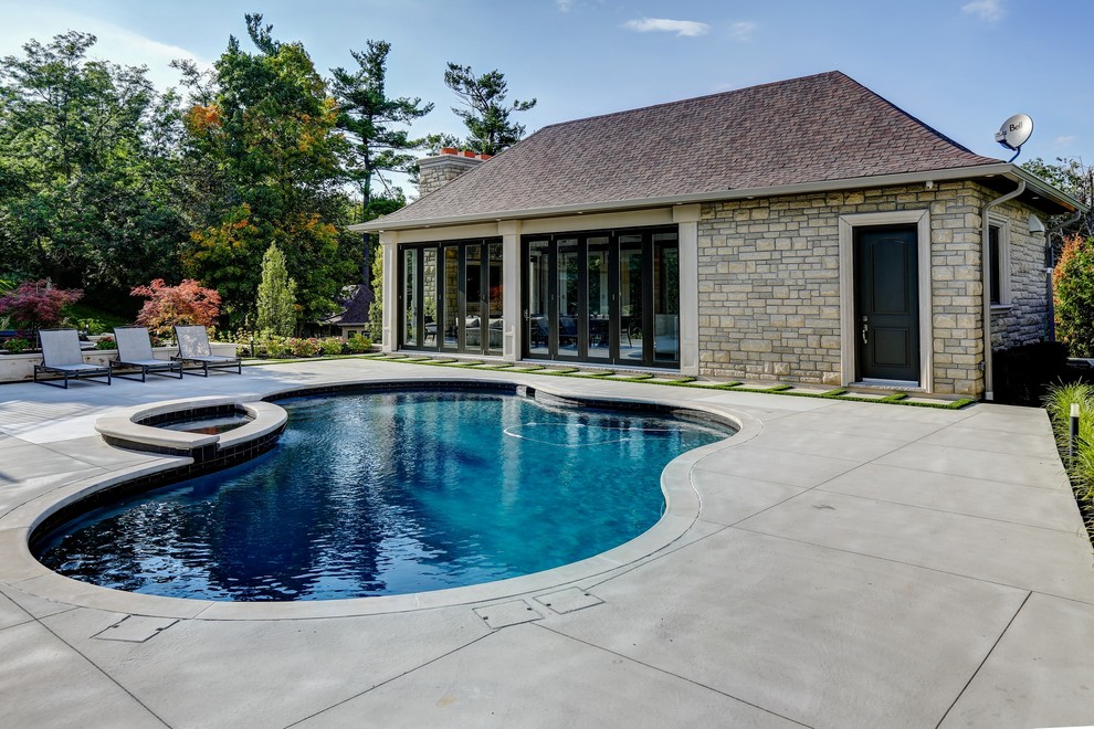 Immagine di una piscina classica a "C" di medie dimensioni e dietro casa con una dépendance a bordo piscina e lastre di cemento