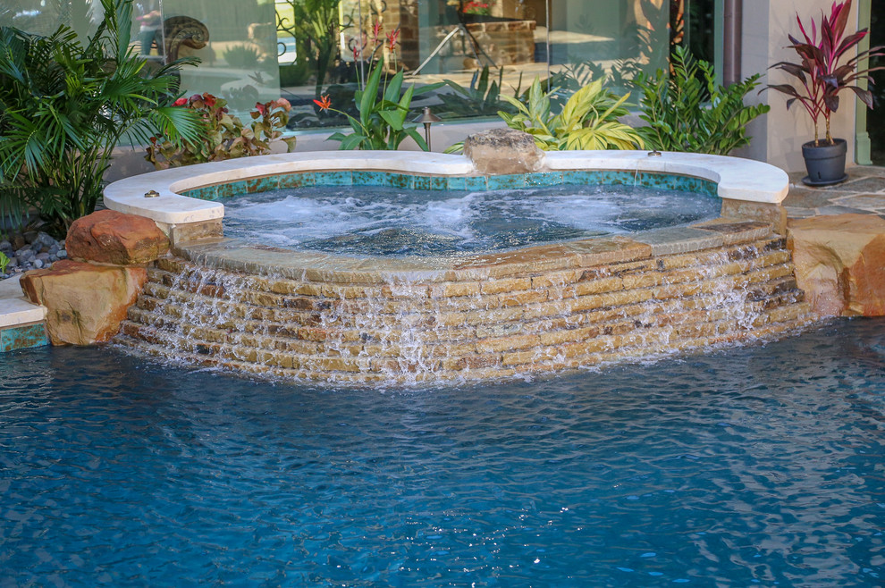 Aménagement d'une piscine méditerranéenne de taille moyenne et sur mesure avec un bain bouillonnant, une cour et des pavés en pierre naturelle.