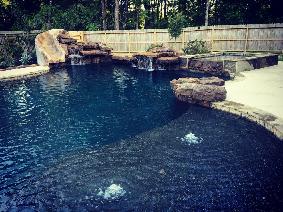 Foto di una grande piscina monocorsia stile americano personalizzata dietro casa con un acquascivolo e pavimentazioni in pietra naturale