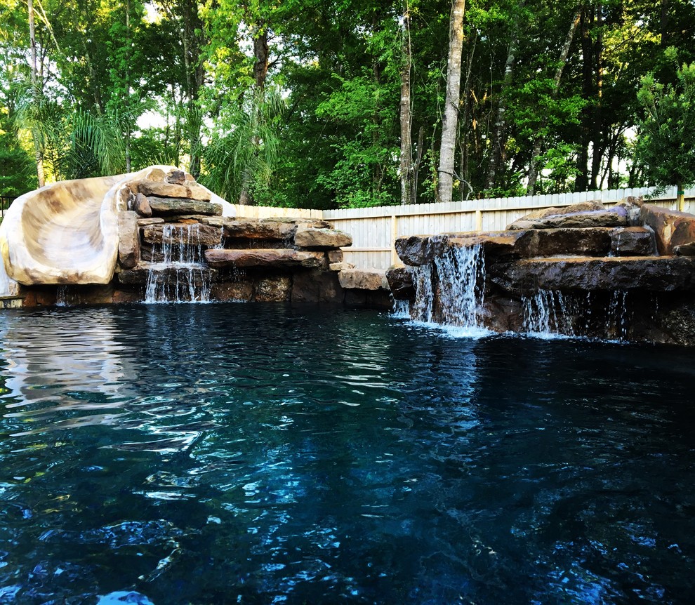 This is an example of a medium sized rustic back custom shaped lengths swimming pool in Houston with a water slide and natural stone paving.