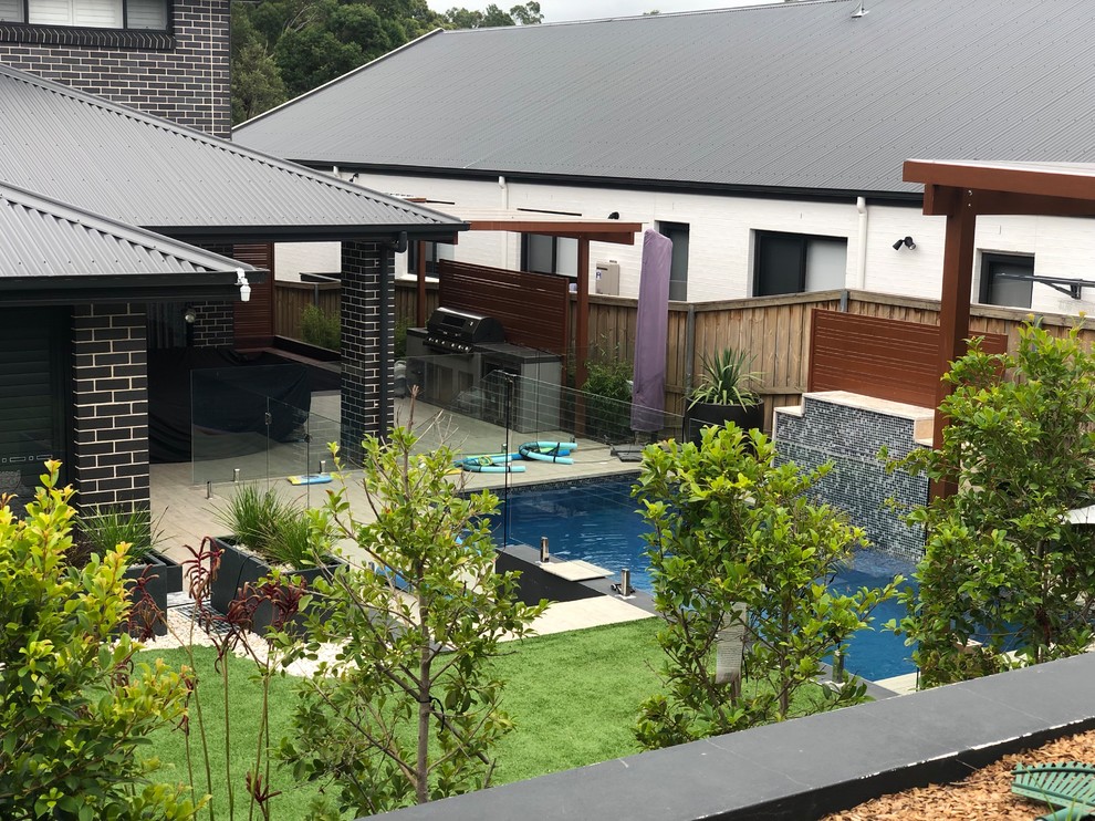 This is an example of a medium sized modern back rectangular natural swimming pool in Sydney with a water feature and tiled flooring.