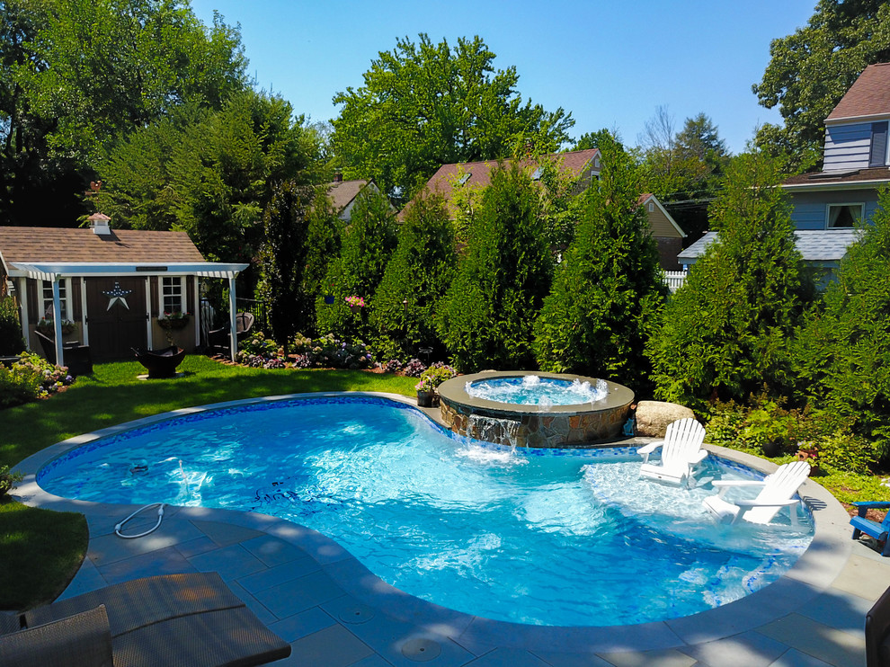Modelo de piscina natural mediterránea de tamaño medio a medida en patio trasero con adoquines de piedra natural