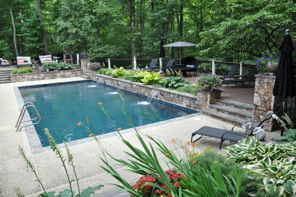 Ispirazione per un'ampia piscina monocorsia stile americano rettangolare dietro casa con fontane e lastre di cemento