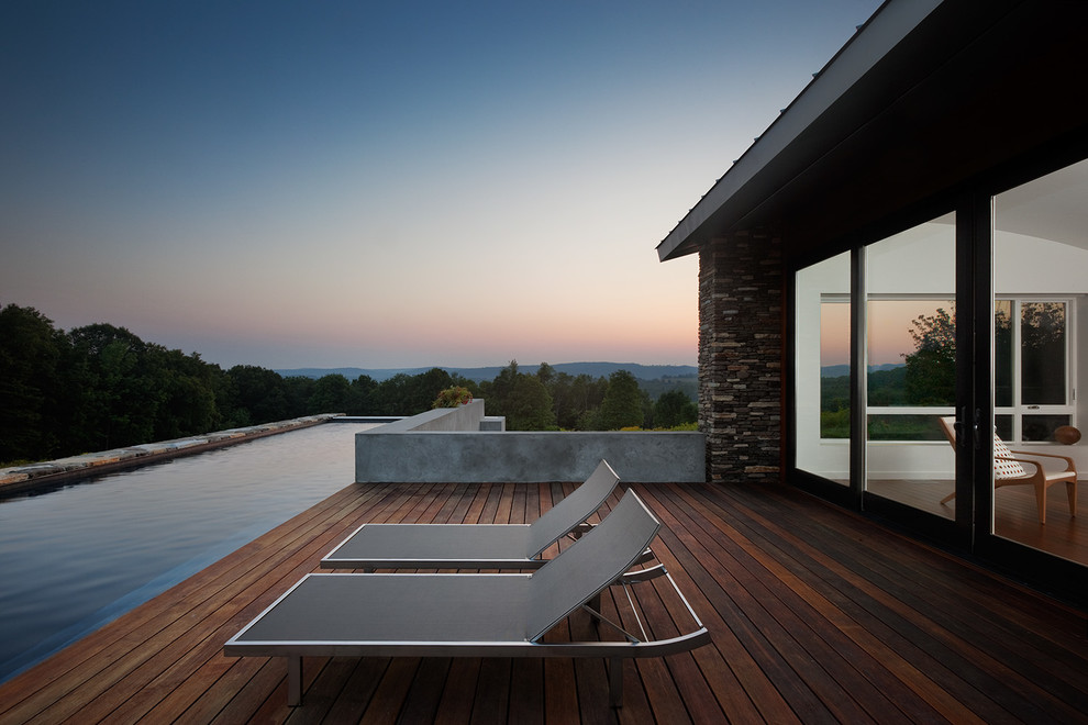 Cette image montre une grande piscine arrière minimaliste rectangle avec une terrasse en bois.