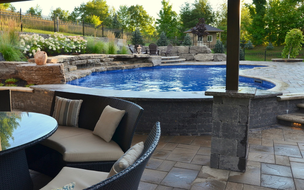 Ejemplo de piscina con fuente marinera grande en patio trasero con adoquines de hormigón