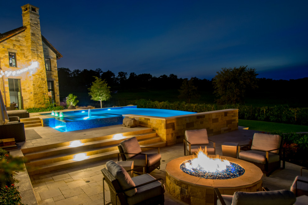 Modelo de piscina con fuente infinita tradicional renovada grande a medida en patio trasero con adoquines de piedra natural