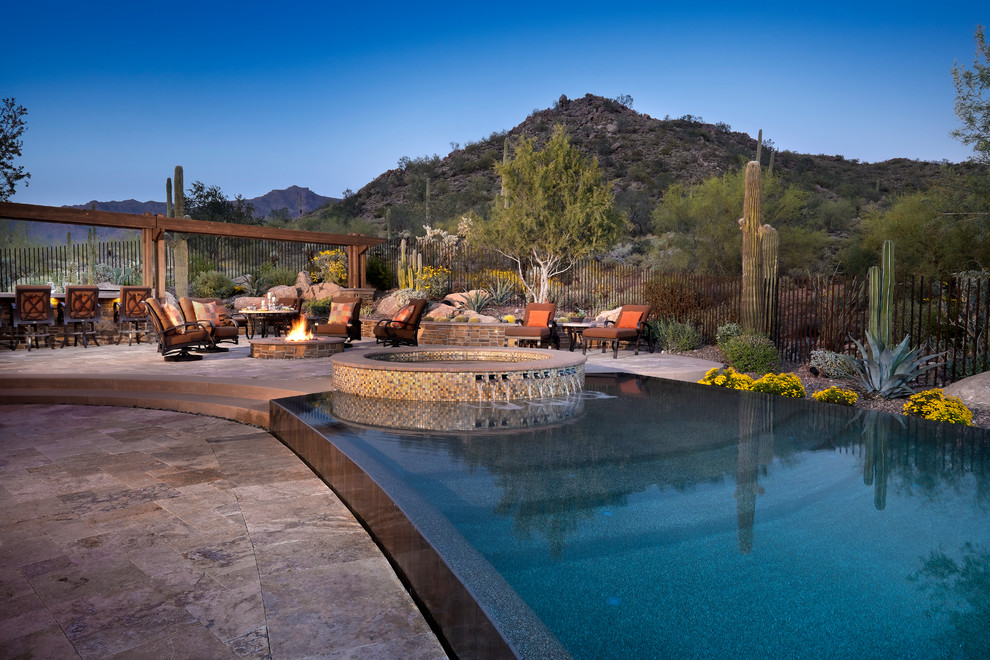 Expansive back custom shaped infinity hot tub in Phoenix with natural stone paving.
