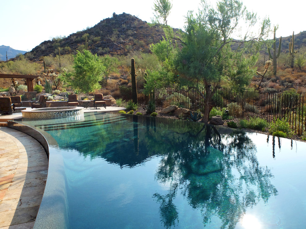 Immagine di un'ampia piscina a sfioro infinito american style personalizzata dietro casa con una vasca idromassaggio e pavimentazioni in pietra naturale