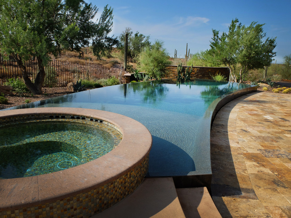 Réalisation d'une très grande piscine à débordement et arrière sud-ouest américain sur mesure avec un bain bouillonnant et des pavés en pierre naturelle.