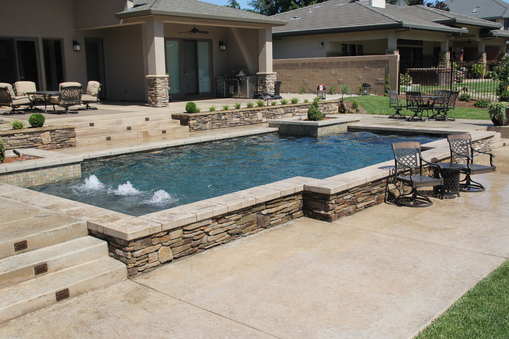 Ejemplo de piscina con fuente elevada actual de tamaño medio rectangular en patio trasero con losas de hormigón