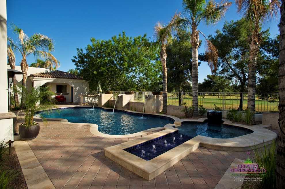 Large modern back custom shaped swimming pool in Phoenix with a water feature and stamped concrete.