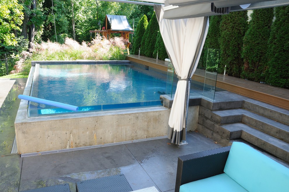 Пример оригинального дизайна: большой наземный, прямоугольный бассейн на заднем дворе в стиле модернизм с фонтаном и покрытием из бетонных плит