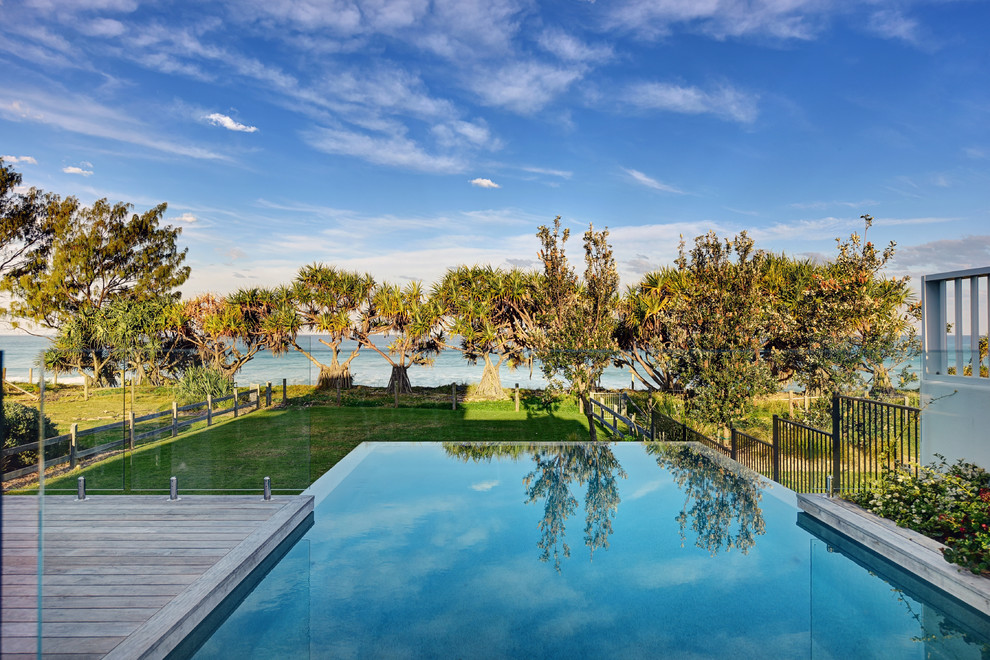 Cette image montre une piscine à débordement et arrière ethnique rectangle avec une terrasse en bois.