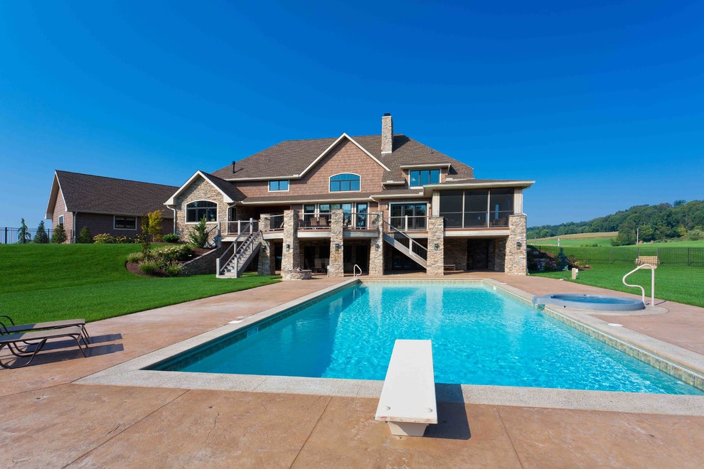 Diseño de piscina alargada campestre grande rectangular en patio trasero con adoquines de hormigón