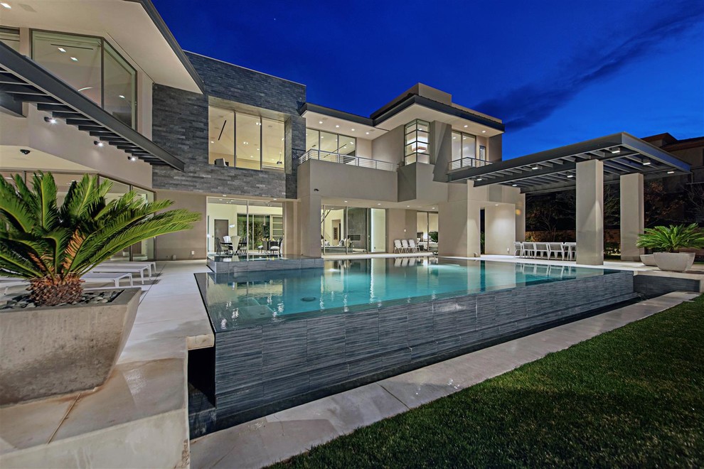 Esempio di una piscina a sfioro infinito design rettangolare di medie dimensioni e dietro casa con una vasca idromassaggio e lastre di cemento