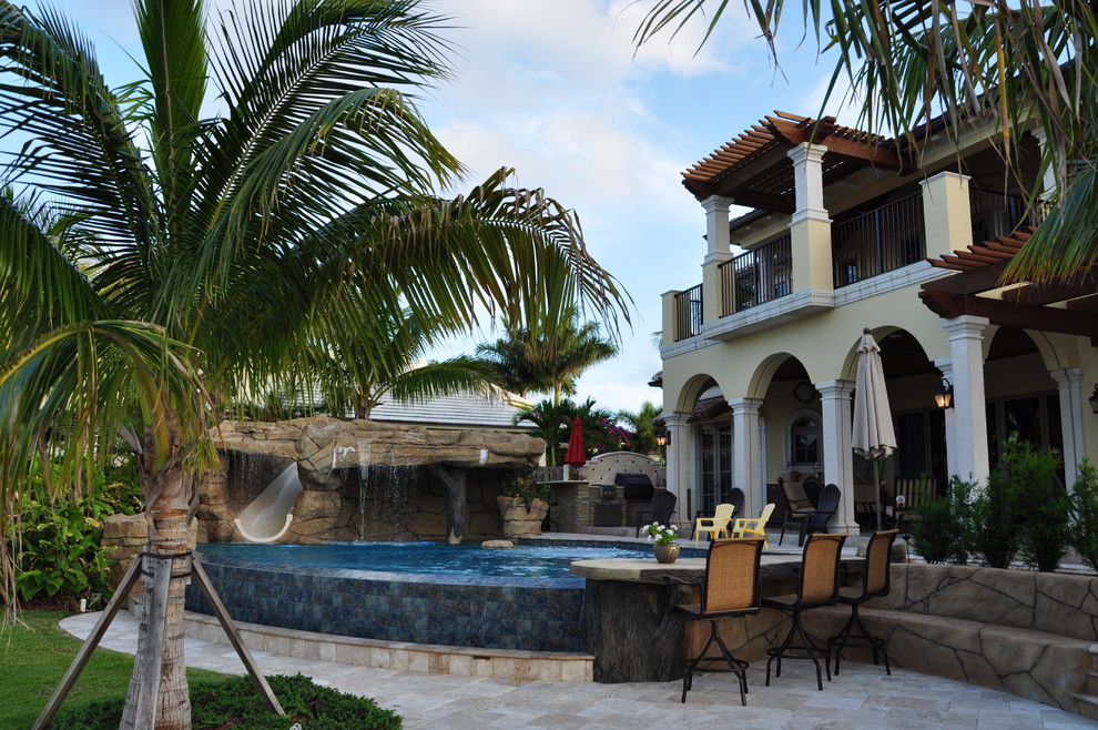 Large mediterranean back custom shaped infinity swimming pool in Miami with natural stone paving.