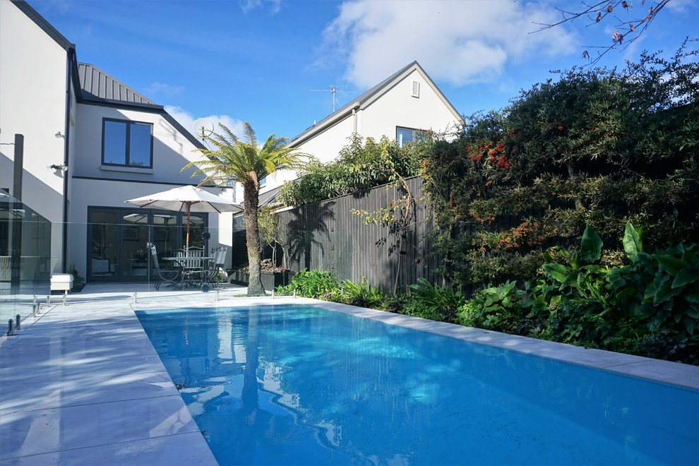 This is an example of a medium sized modern back swimming pool in Christchurch with natural stone paving.