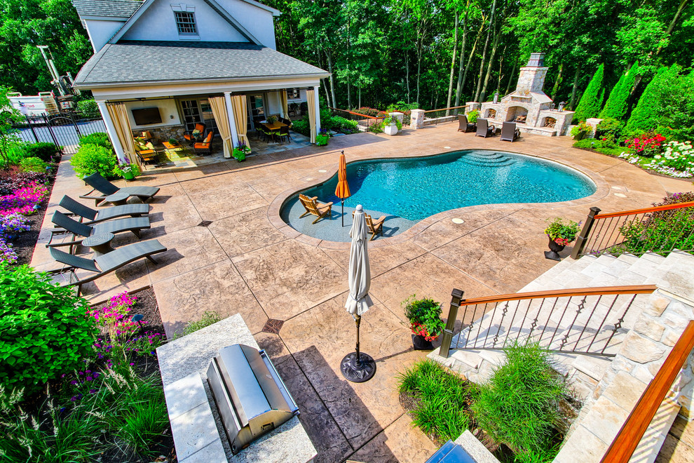 Ejemplo de piscina natural tradicional renovada de tamaño medio a medida en patio trasero con suelo de hormigón estampado