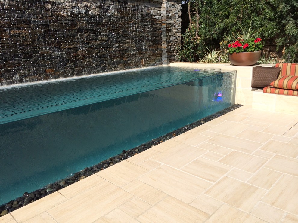 Immagine di una piscina a sfioro infinito rettangolare di medie dimensioni e dietro casa con fontane e piastrelle