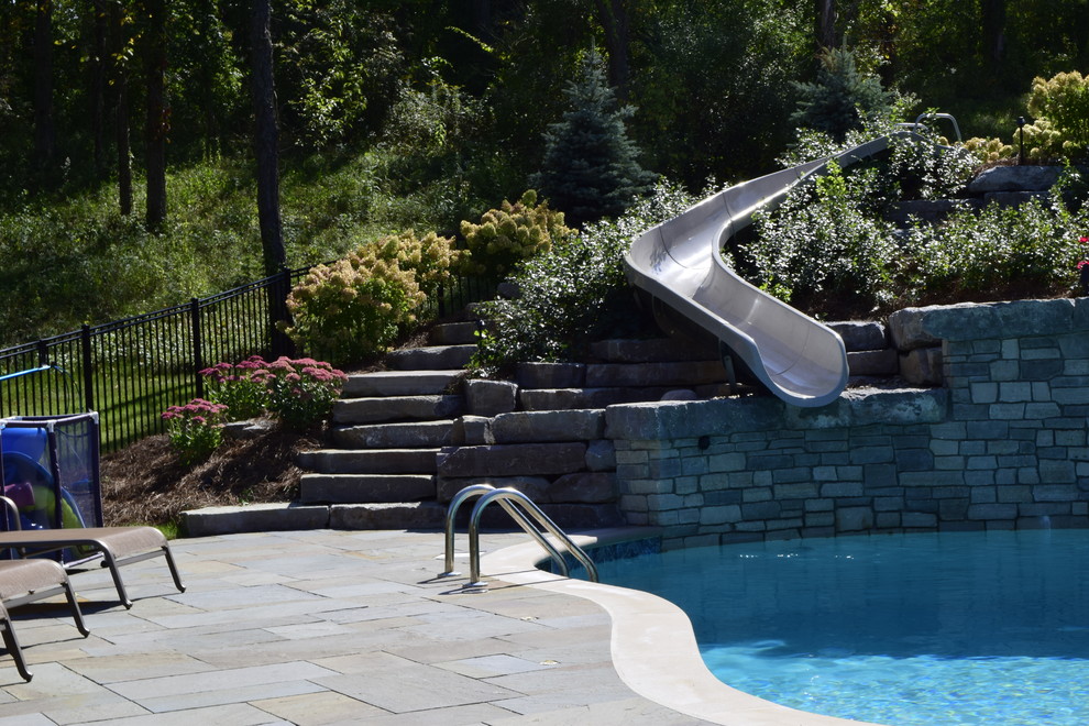 Modelo de piscina con tobogán tradicional renovada grande a medida en patio trasero con adoquines de piedra natural