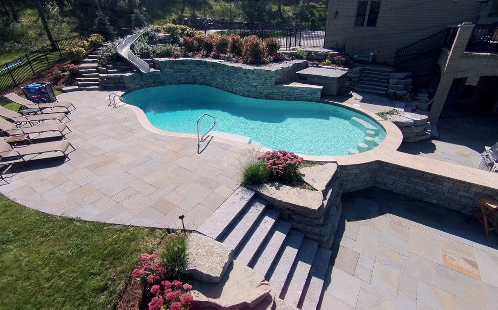 Diseño de piscina con tobogán tradicional renovada grande a medida en patio trasero con adoquines de piedra natural
