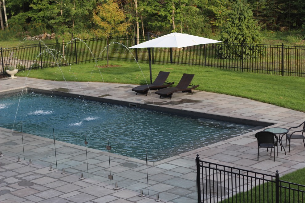 Modelo de piscina con fuente alargada moderna grande rectangular en patio trasero con suelo de hormigón estampado