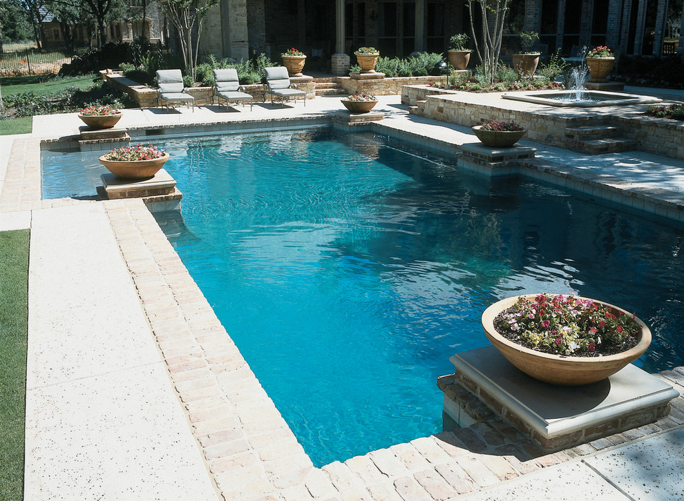 Ejemplo de piscina con fuente clásica grande en forma de L en patio trasero con adoquines de ladrillo