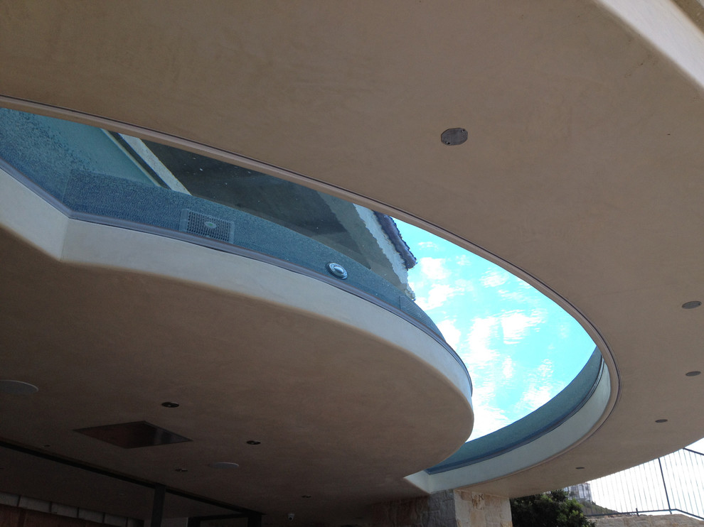 Diseño de piscina infinita actual grande a medida en patio trasero con adoquines de ladrillo