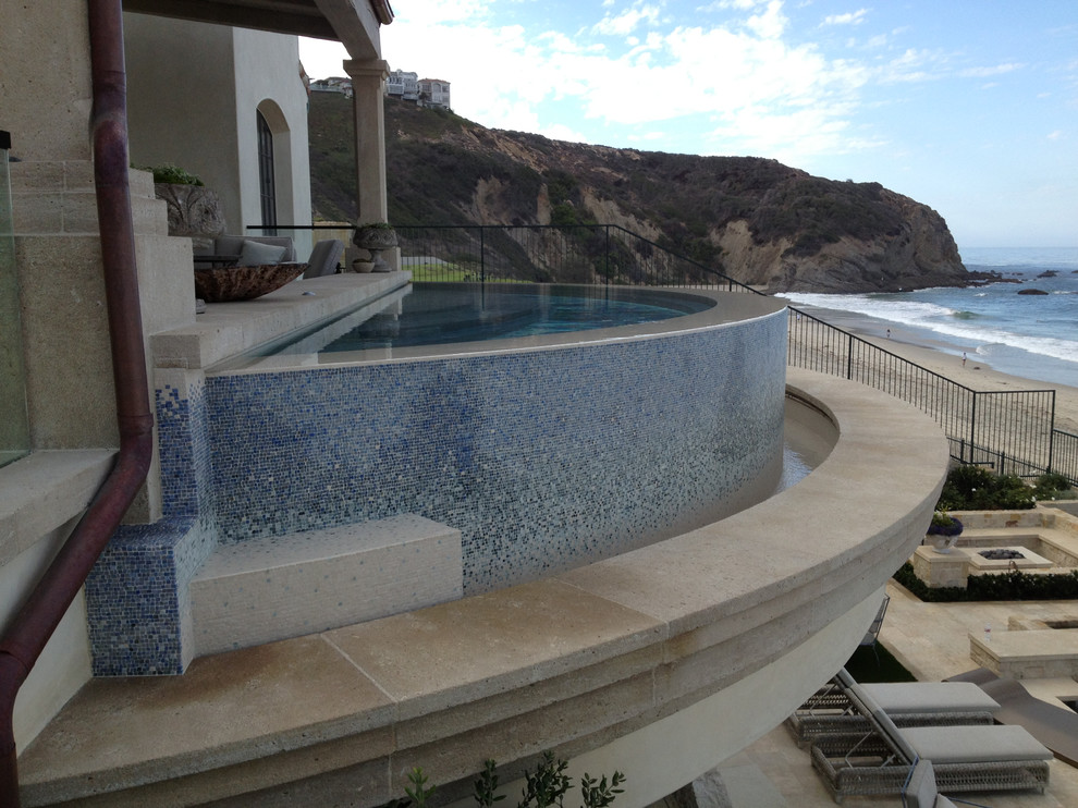 This is an example of a large contemporary back custom shaped infinity swimming pool in Other with brick paving.