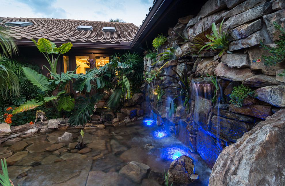 Ejemplo de piscina con fuente natural tropical grande a medida en patio lateral con adoquines de piedra natural
