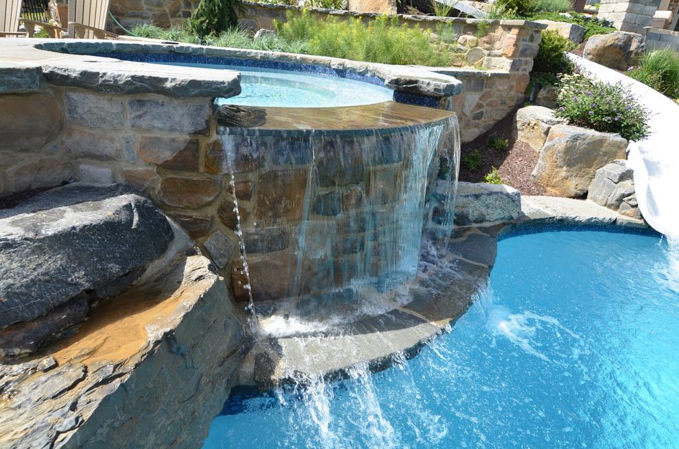 Idée de décoration pour une grande piscine arrière design sur mesure avec un toboggan et des pavés en pierre naturelle.