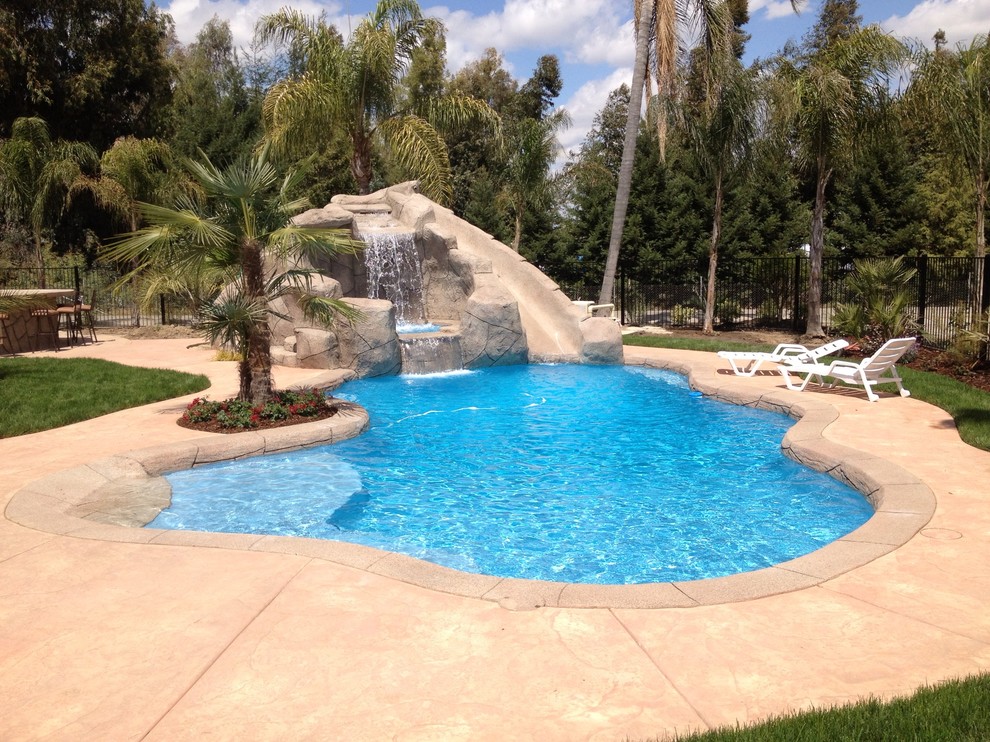 Modelo de piscina con tobogán exótica grande a medida en patio trasero con suelo de hormigón estampado