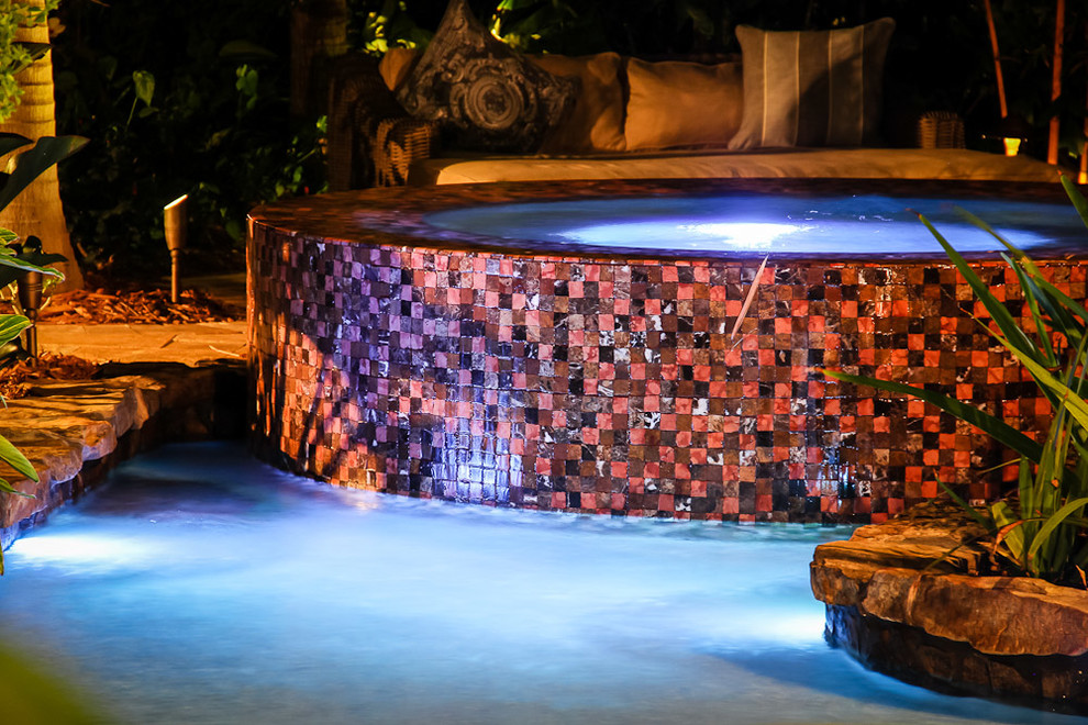 Ejemplo de piscina con fuente alargada exótica extra grande a medida en patio trasero con adoquines de piedra natural