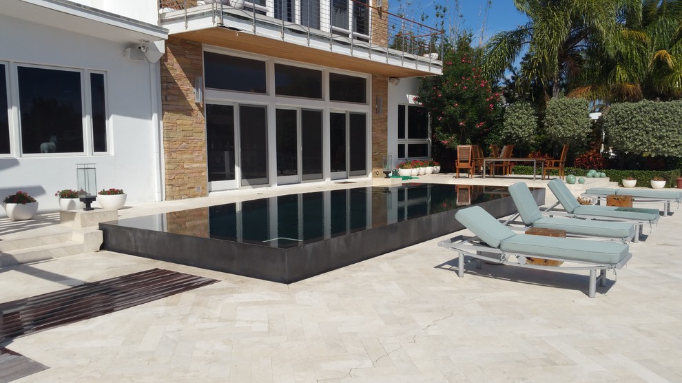 Imagen de piscina infinita minimalista grande a medida en patio trasero con adoquines de piedra natural