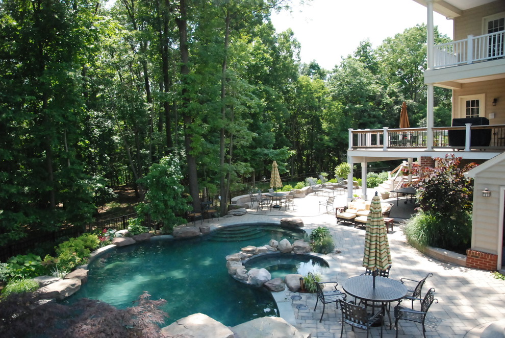 Imagen de piscina natural tradicional grande a medida en patio trasero con adoquines de hormigón