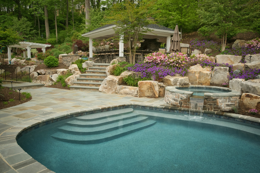 Diseño de piscina clásica grande redondeada en patio trasero con adoquines de piedra natural