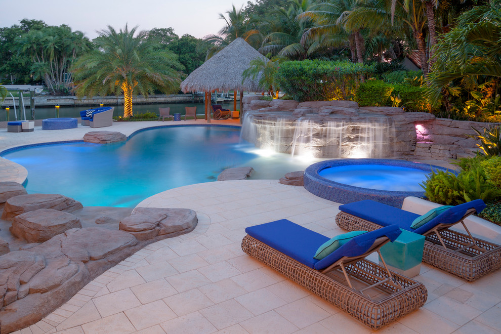 Design ideas for a large world-inspired back custom shaped swimming pool in Tampa with a water feature and natural stone paving.